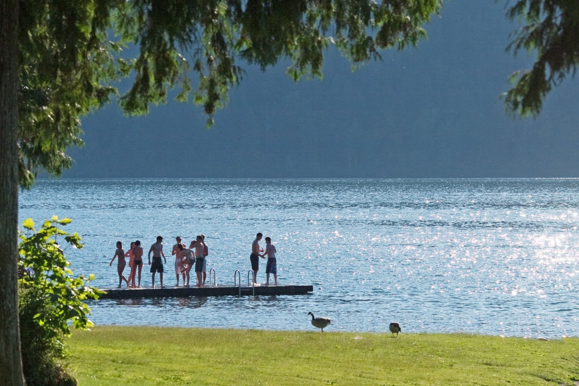 Campers on a swim dock against sunlit lake water